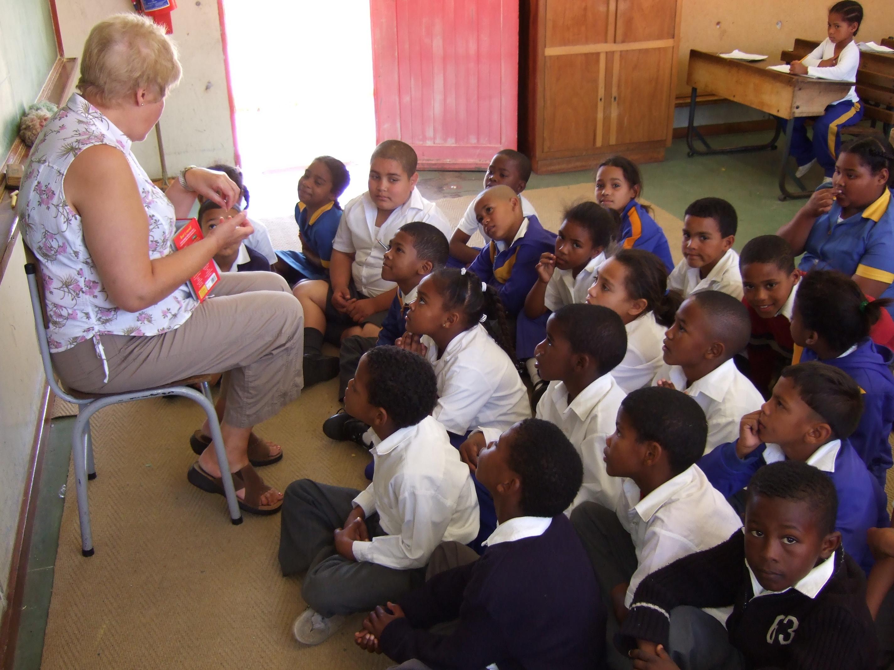 An older volunteer reading a book to her students during her teaching work experience in South Africa Young students listen to a Projects Abroad volunteer as a teacher in South Africa